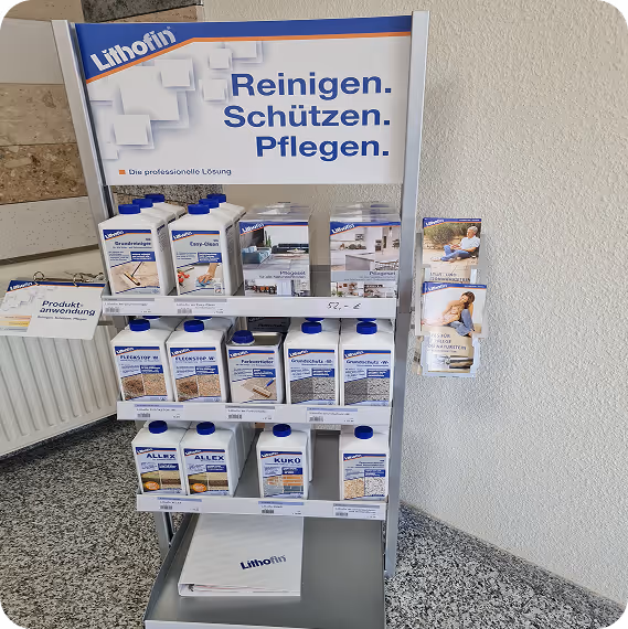 Verkaufsregal mit Lithofin Reinigungs- und Pflegeprodukten in weißen Behältern plus Produktanwendungsbroschüren an der Wand.