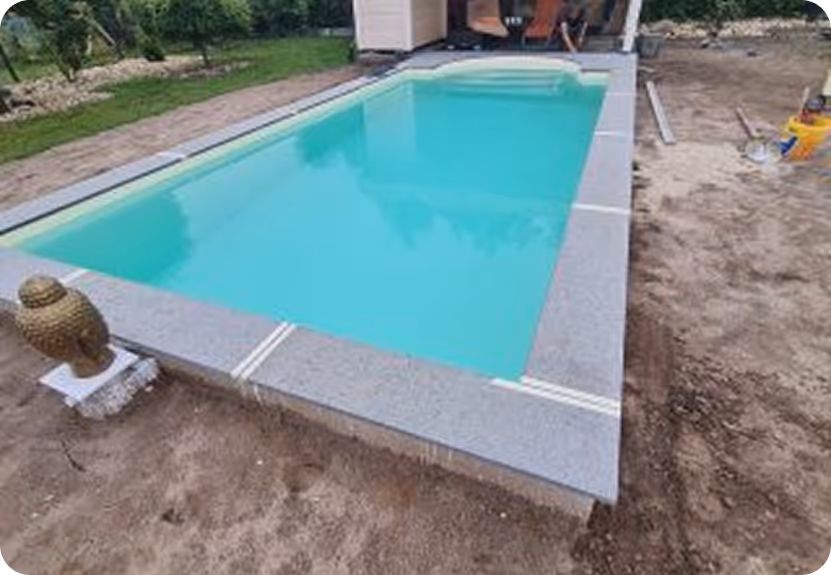 Kleiner rechteckiger Swimmingpool mit klar blauem Wasser und grauer Umrandung aus Fliesen, umgeben von Erde und Gartenbereich.