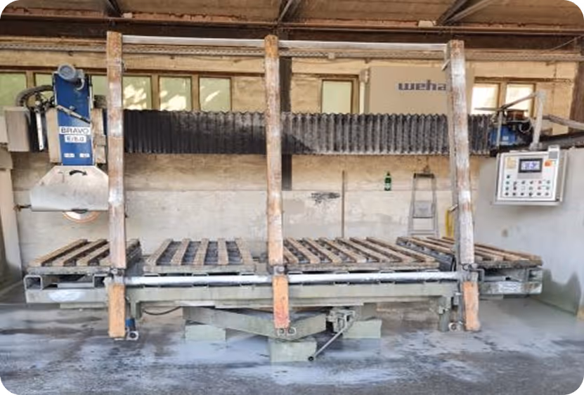 Industrielle 5-Achs-CNC-Brückensäge mit Steuerung in einer Werkstatt mit Staub und Gebrauchsspuren.
